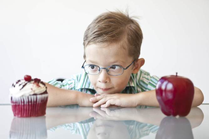 Little boy choosing between a cupcake and apple